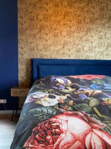Slaapkamerinspiratie: masterbedroom goudkleurig behang en blauw bed met kleurrijk beddengoed